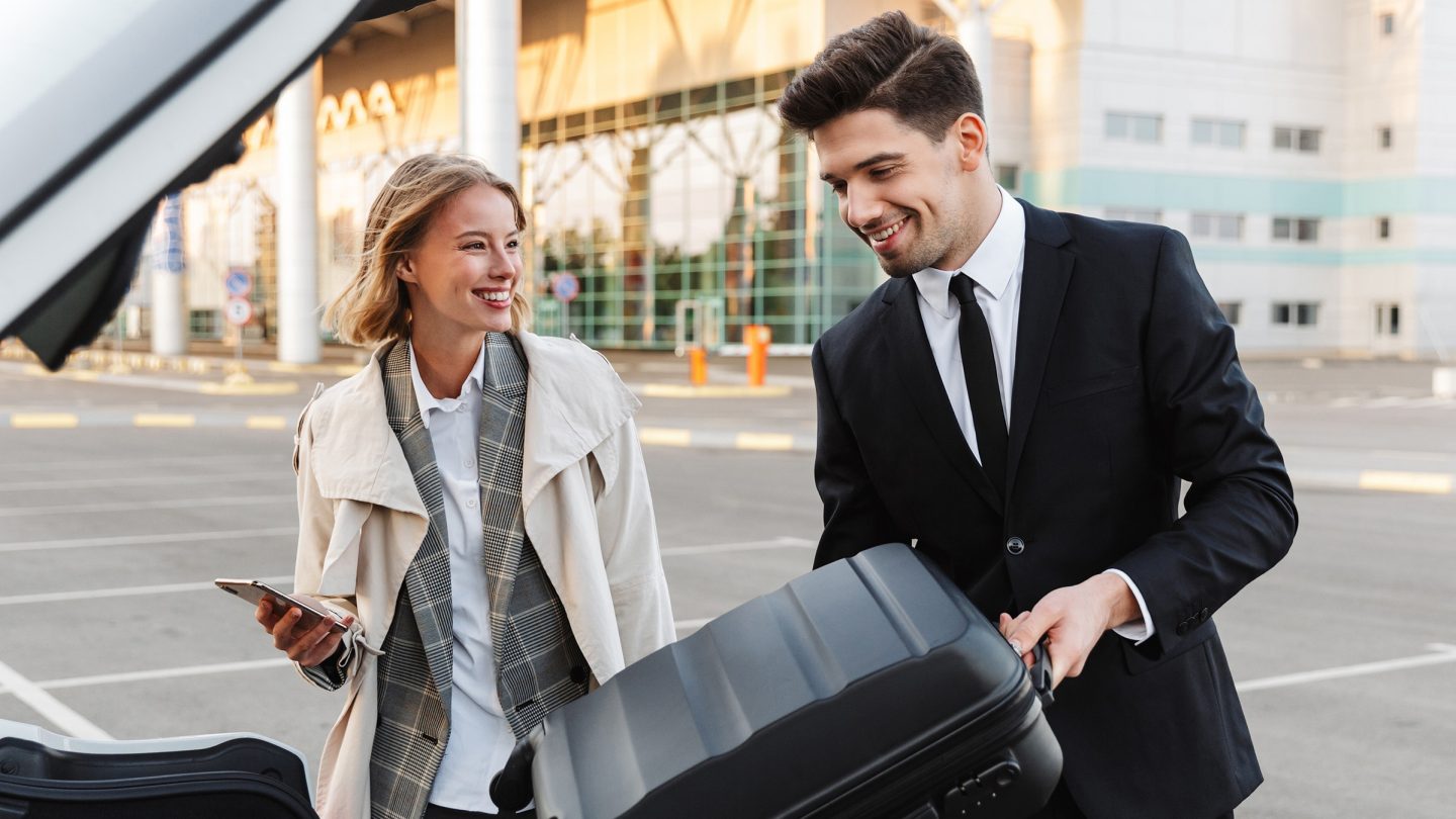 A man loads a woman’s suitcase into a car