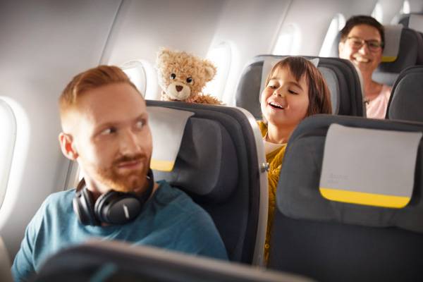 A child is sitting in Economy Class with her teddy bear